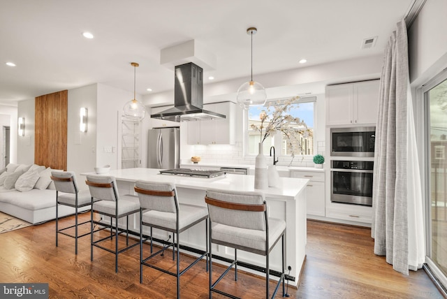 kitchen with wood finished floors, island exhaust hood, visible vents, and stainless steel appliances