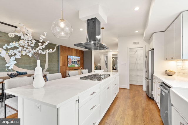 kitchen featuring light wood finished floors, stainless steel appliances, light countertops, white cabinets, and island range hood