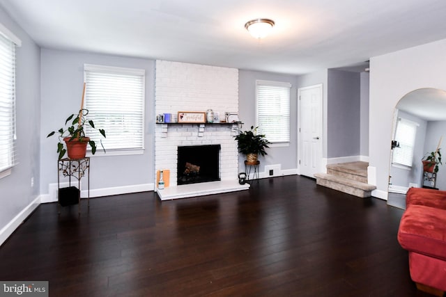 living room featuring a fireplace, baseboards, arched walkways, and wood finished floors