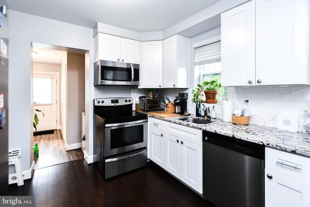 kitchen with dark wood-style flooring, a sink, white cabinetry, appliances with stainless steel finishes, and tasteful backsplash