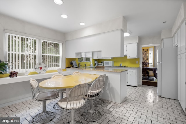 kitchen featuring recessed lighting, white appliances, brick floor, and white cabinets