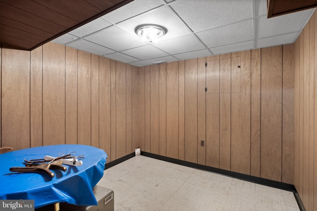 empty room with a paneled ceiling, light floors, and wooden walls