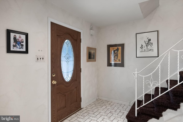 foyer entrance featuring brick floor, stairway, and baseboards