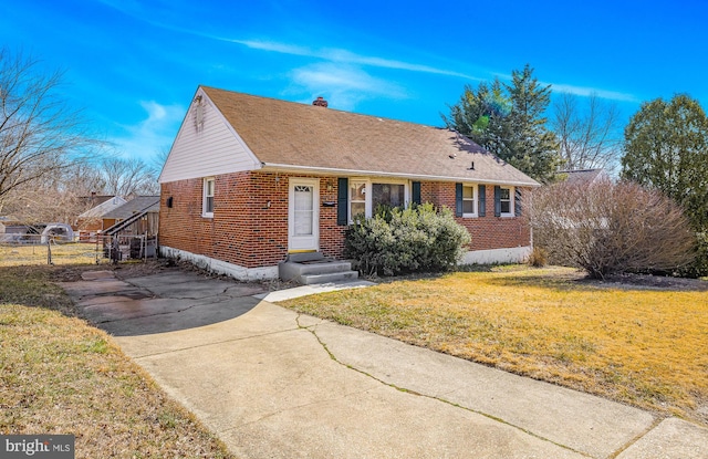 view of front of house with a front lawn, fence, a shingled roof, brick siding, and a chimney