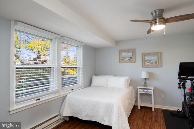 bedroom with a baseboard heating unit, dark wood-type flooring, and baseboards