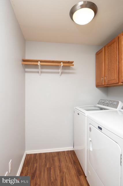 clothes washing area featuring cabinet space, baseboards, washer and clothes dryer, and wood finished floors