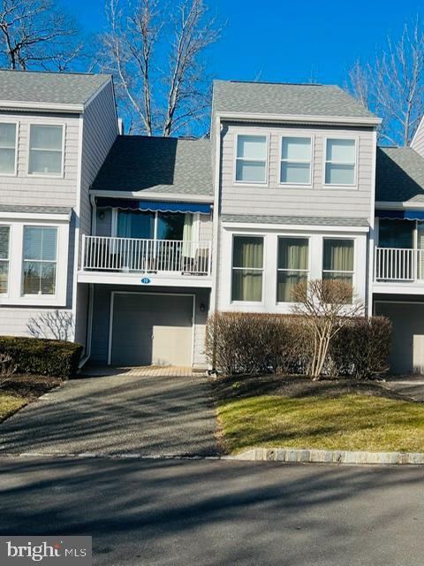 view of front of property with aphalt driveway, roof with shingles, a balcony, and a garage