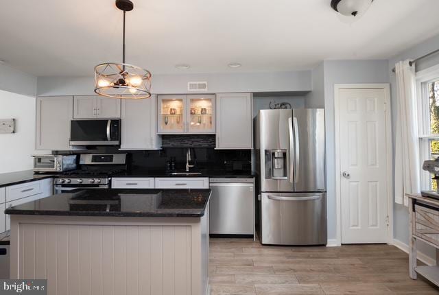 kitchen featuring light wood-style flooring, a sink, hanging light fixtures, appliances with stainless steel finishes, and tasteful backsplash