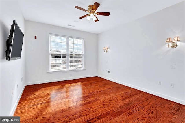 unfurnished room with a ceiling fan, wood finished floors, visible vents, and baseboards