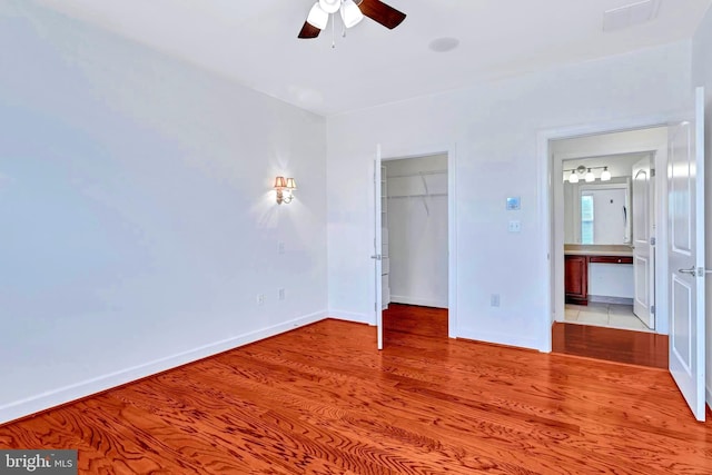 unfurnished bedroom with a walk in closet, a closet, baseboards, and light wood finished floors