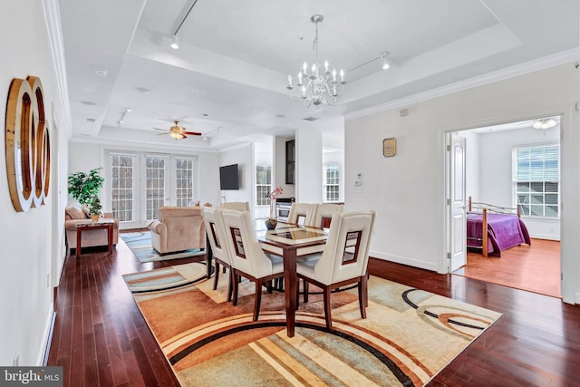 dining space with ceiling fan with notable chandelier, hardwood / wood-style floors, a raised ceiling, and baseboards