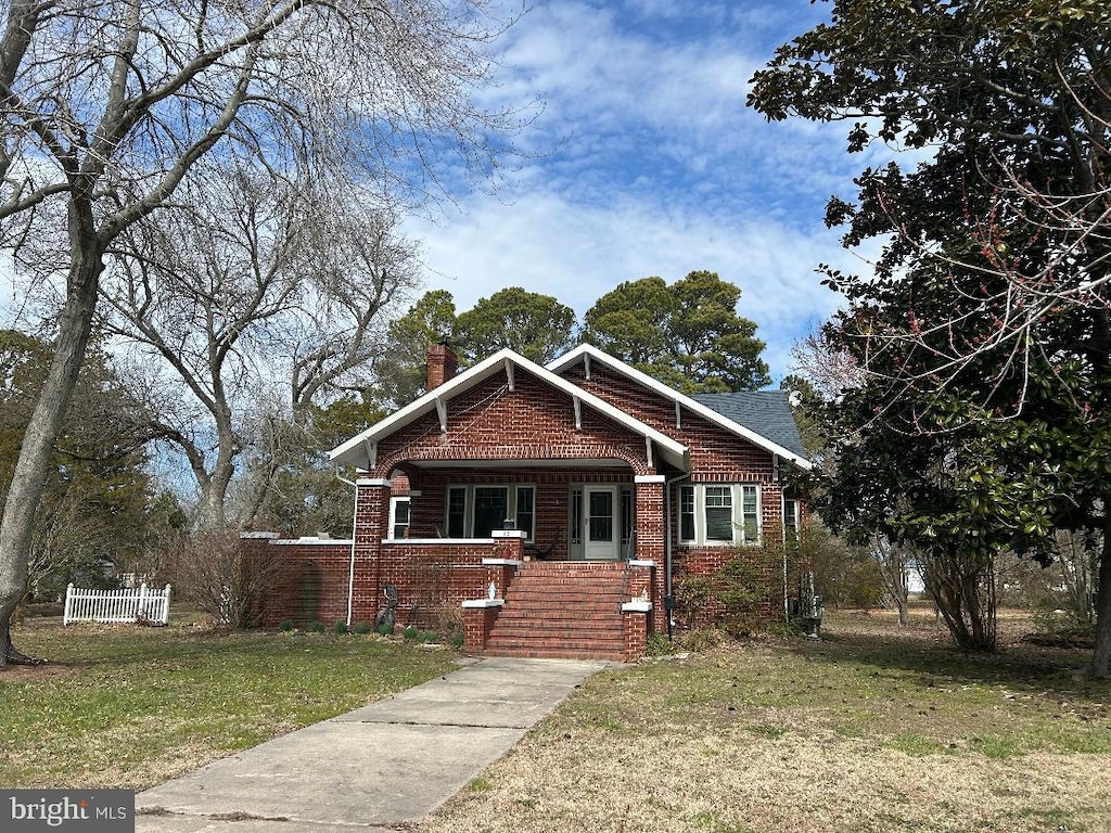 view of front facade with a front yard, brick siding, fence, and a chimney