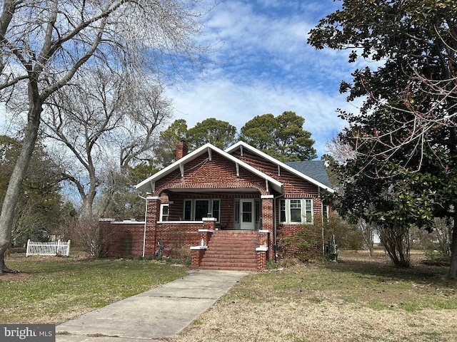 view of front facade with a front yard, brick siding, fence, and a chimney