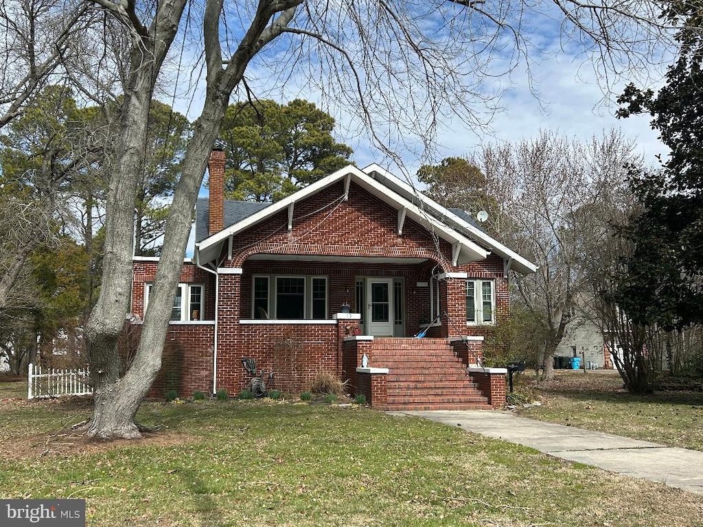 view of front of property featuring a front yard, a chimney, and brick siding