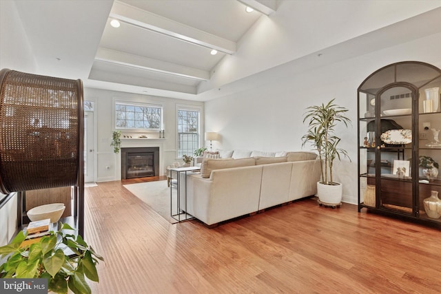 living room featuring lofted ceiling with beams, light wood-style flooring, recessed lighting, baseboards, and a glass covered fireplace