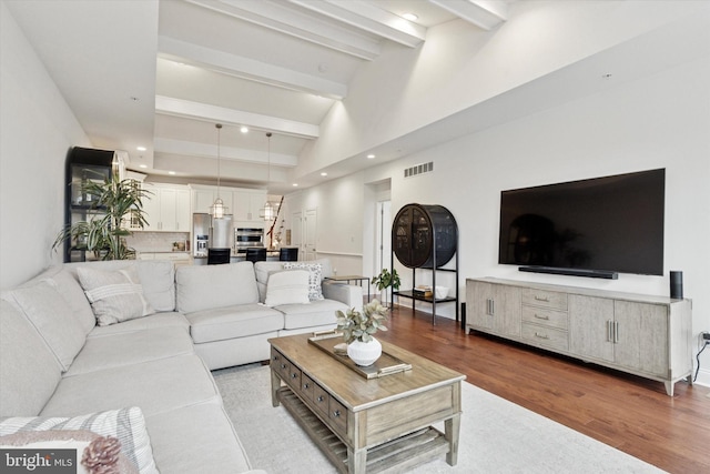 living area featuring beam ceiling, recessed lighting, visible vents, a high ceiling, and wood finished floors