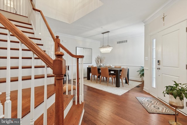 entrance foyer with visible vents, dark wood-style floors, ornamental molding, an inviting chandelier, and stairs