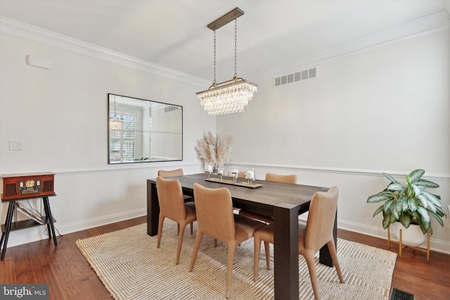 dining area featuring crown molding, a notable chandelier, visible vents, wood finished floors, and baseboards