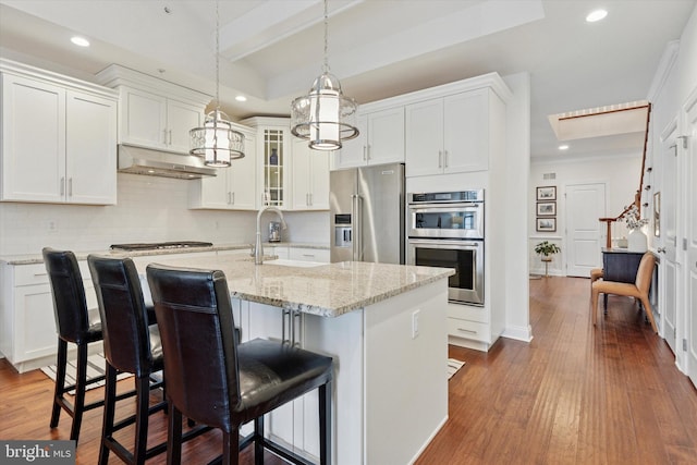 kitchen with appliances with stainless steel finishes, dark wood-style flooring, a sink, and under cabinet range hood