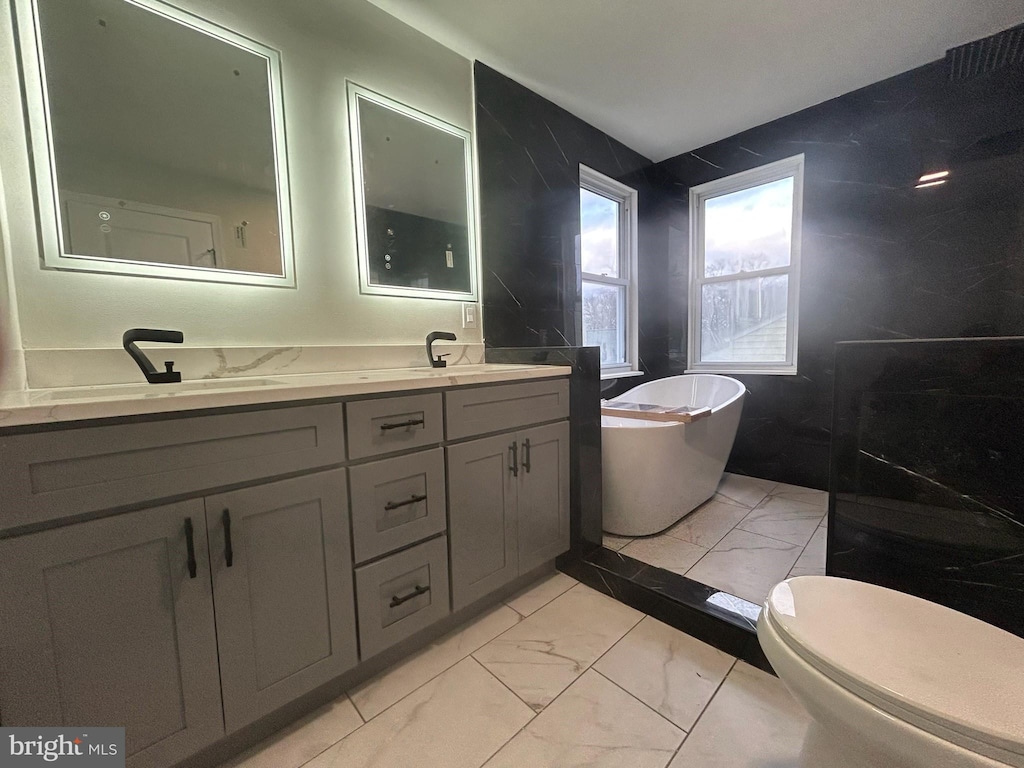 full bathroom featuring double vanity, a sink, a freestanding bath, toilet, and marble finish floor