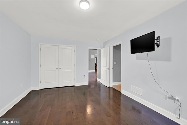 unfurnished bedroom with a closet, dark wood finished floors, visible vents, and baseboards