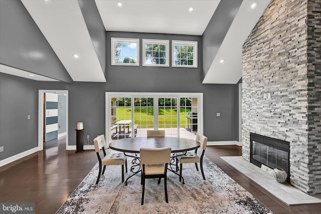 dining area with a stone fireplace, wood finished floors, a high ceiling, and baseboards