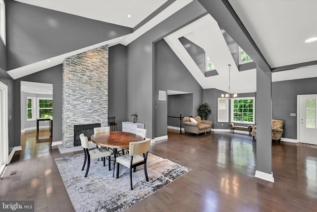 dining area featuring baseboards, wood finished floors, an inviting chandelier, a stone fireplace, and high vaulted ceiling