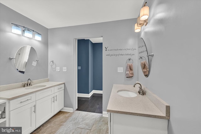 full bath with two vanities, a sink, and baseboards