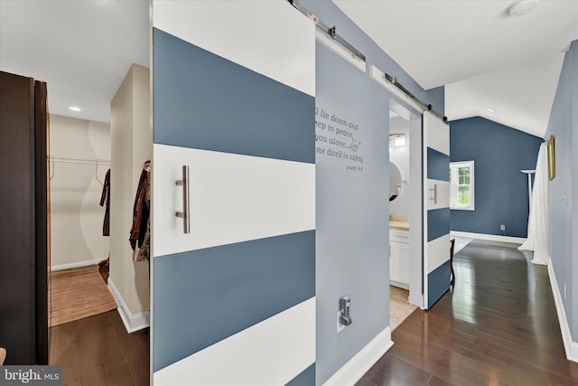 hallway featuring lofted ceiling, dark wood-style floors, a barn door, and baseboards