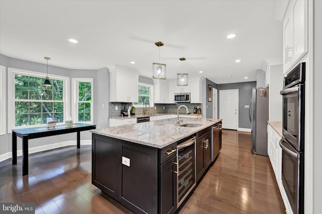 kitchen with a sink, white cabinetry, appliances with stainless steel finishes, backsplash, and an island with sink