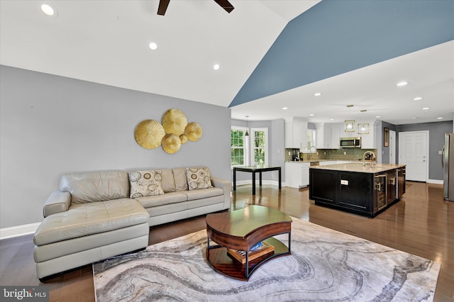 living area with ceiling fan, high vaulted ceiling, recessed lighting, dark wood-style flooring, and baseboards