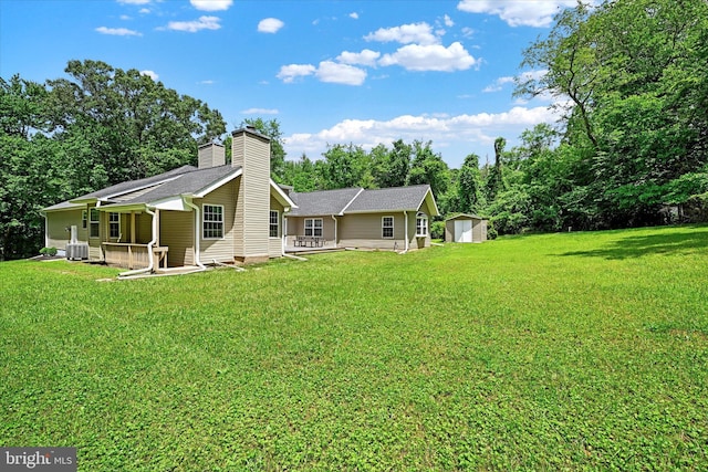 back of house featuring a storage shed, central AC unit, a lawn, a chimney, and an outbuilding