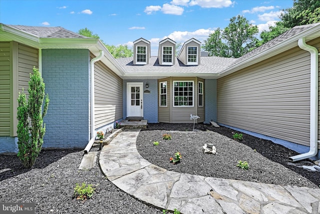 doorway to property with a shingled roof and brick siding