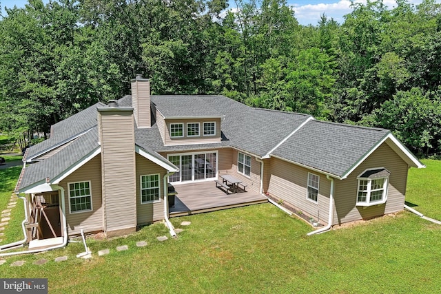 rear view of house with a deck, roof with shingles, a lawn, and a chimney