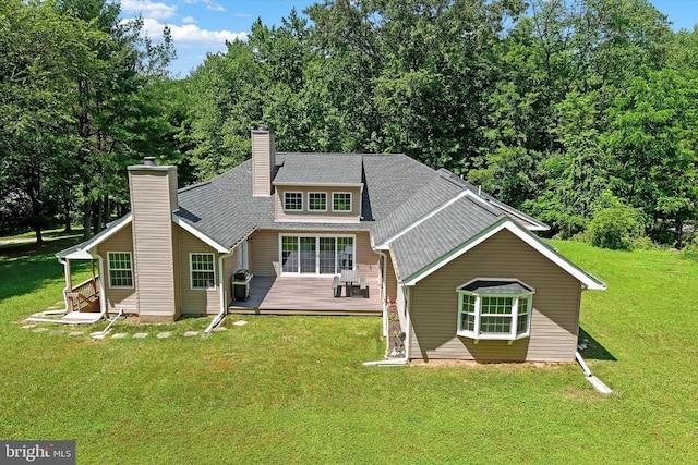 rear view of house with a wooden deck, a chimney, a shingled roof, and a yard