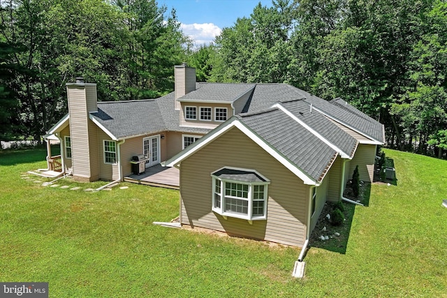 back of house featuring a chimney, a deck, a lawn, and roof with shingles