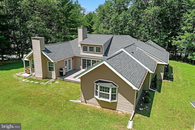 rear view of property featuring a shingled roof, a chimney, a lawn, and a wooden deck