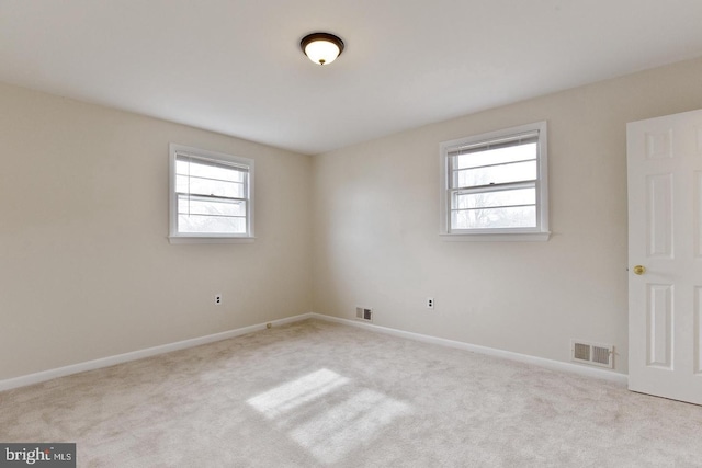 carpeted spare room with a healthy amount of sunlight, visible vents, and baseboards