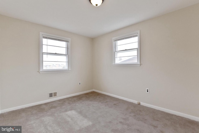 carpeted empty room featuring visible vents, a wealth of natural light, and baseboards