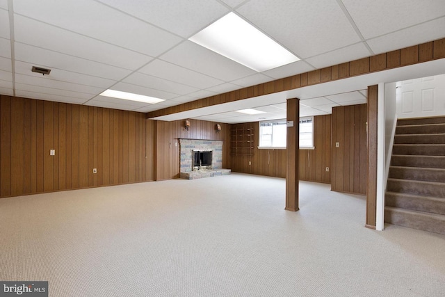 below grade area with a brick fireplace, carpet flooring, wooden walls, and stairs