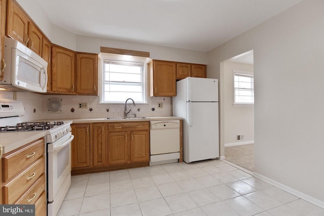 kitchen featuring brown cabinets, light countertops, backsplash, a sink, and white appliances