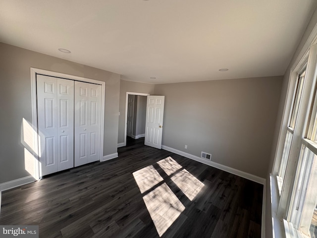 unfurnished bedroom featuring dark wood-style floors, baseboards, visible vents, and a closet