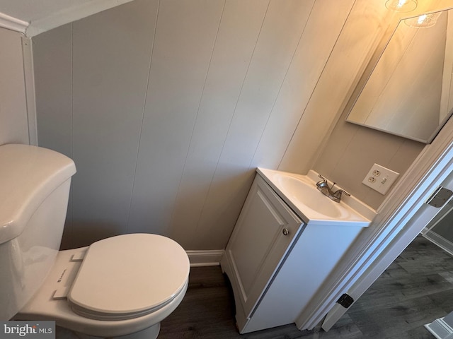 bathroom with toilet, a decorative wall, wood finished floors, and vanity