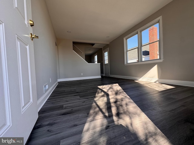 unfurnished living room with stairs, dark wood finished floors, and baseboards