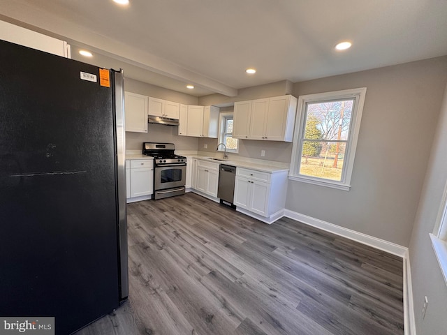 kitchen featuring light countertops, appliances with stainless steel finishes, a sink, under cabinet range hood, and baseboards