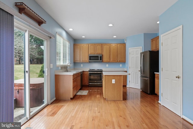 kitchen with light wood-style flooring, a sink, light countertops, appliances with stainless steel finishes, and a center island