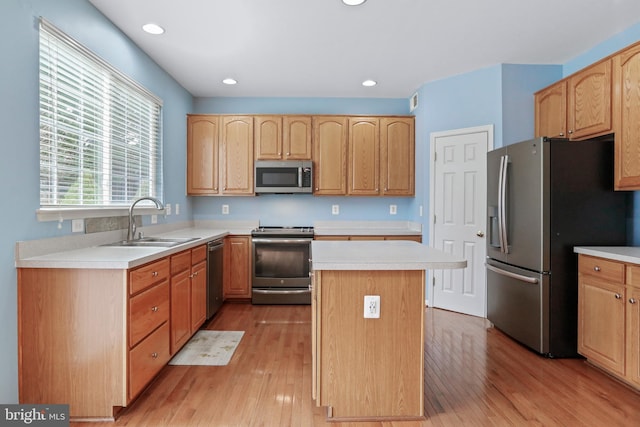 kitchen with a sink, light wood-type flooring, appliances with stainless steel finishes, and light countertops