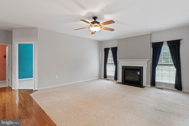 unfurnished living room with visible vents, a fireplace with flush hearth, a ceiling fan, and baseboards