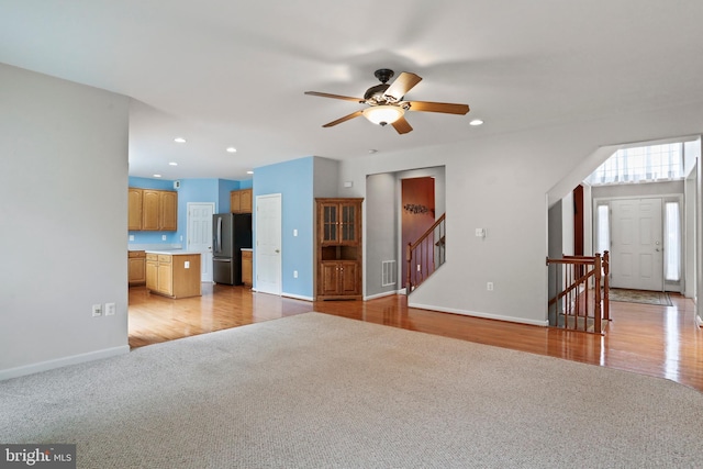 unfurnished living room with light carpet, recessed lighting, light wood-style floors, baseboards, and ceiling fan