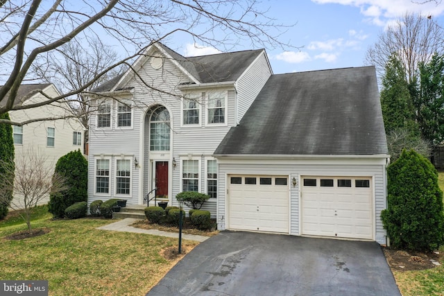 traditional-style house with a front yard, a garage, driveway, and a shingled roof